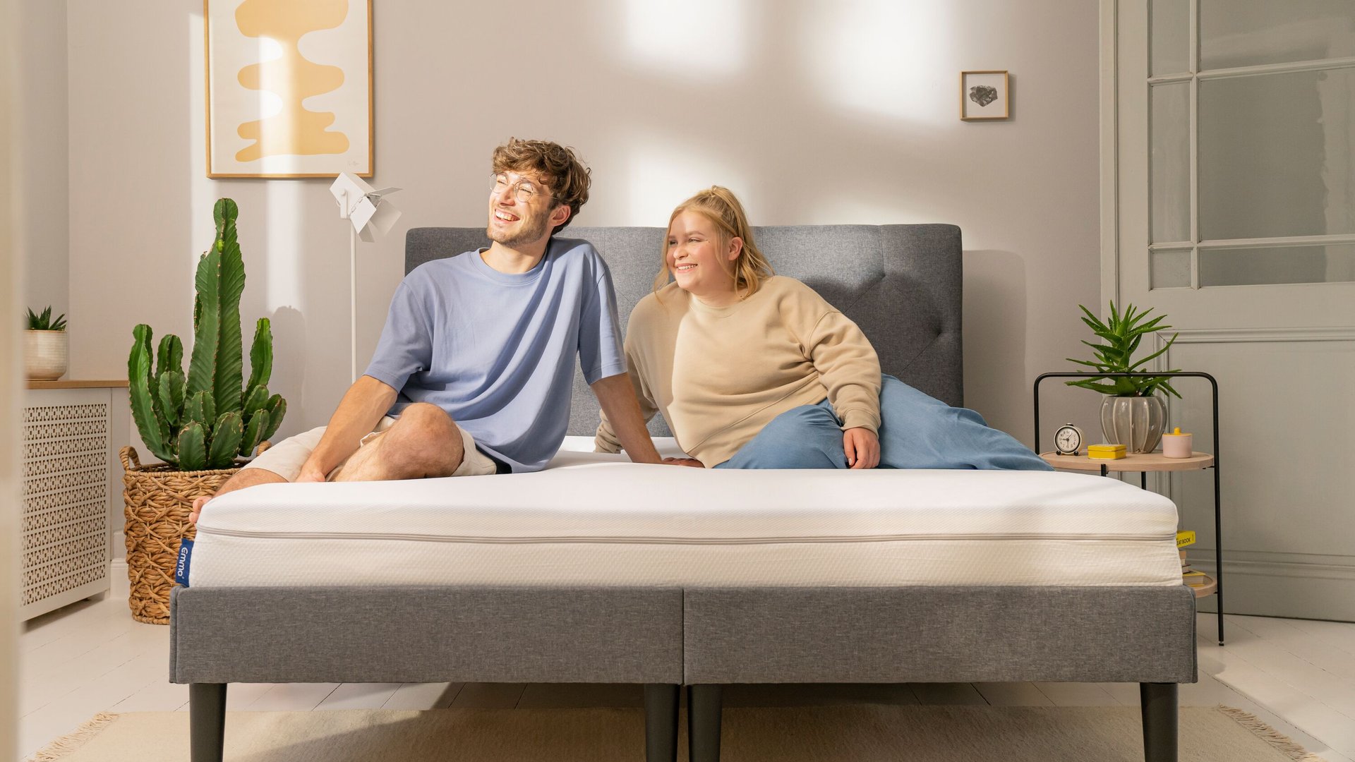 Junges Paar sitzt entspannt auf Emma Boxspringbett in sonnigem Zimmer.